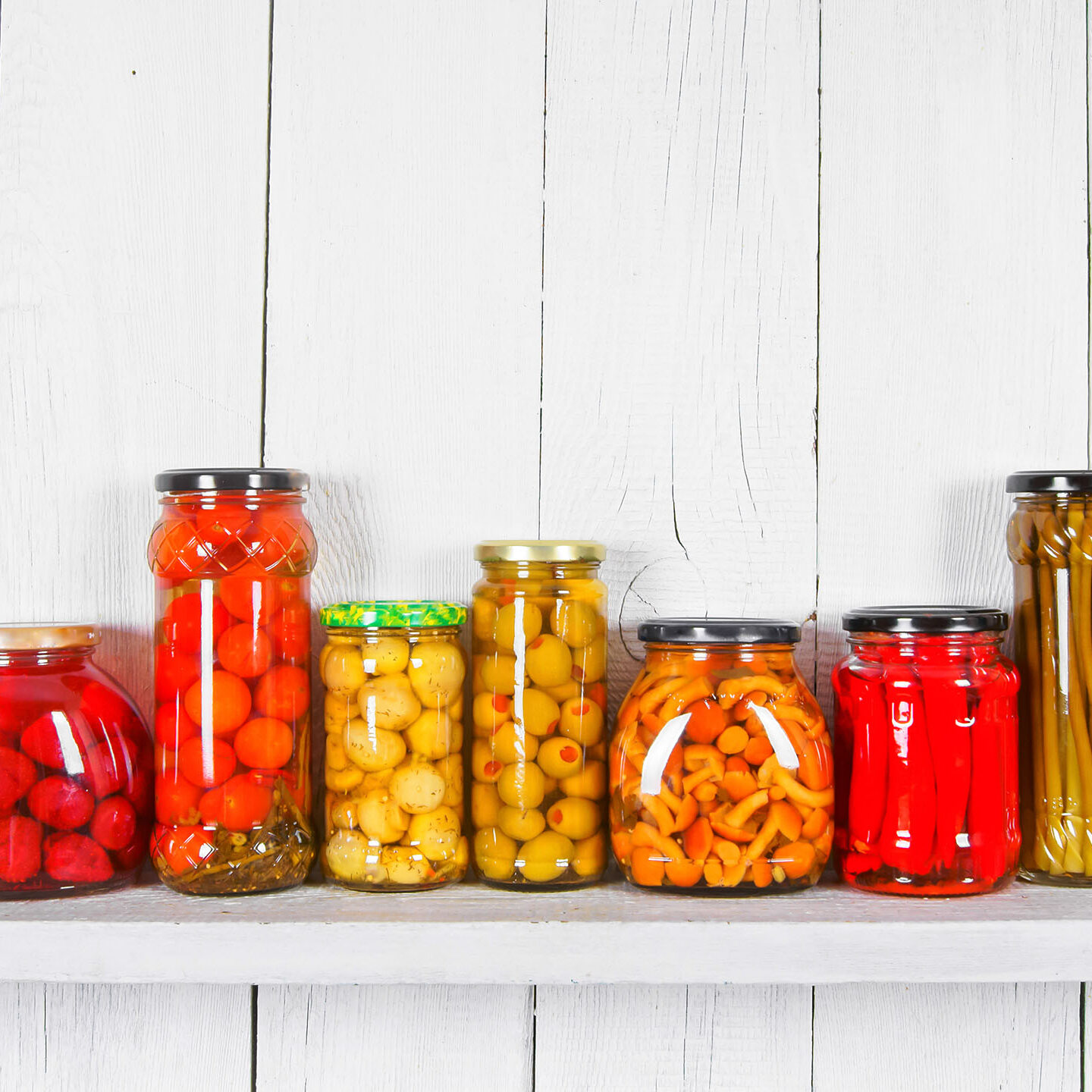 Preserved food in glass jars, on a wooden shelf. Various marinaded food