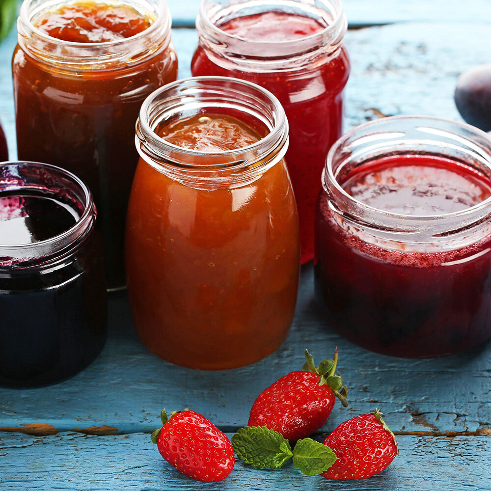 Glass jars with different kinds of jam and berries on wooden table